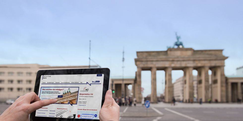 Das Brandenburger Tor im Hintergrund und im vordergrund und ein hochgehaltenes Tablet mit einer website