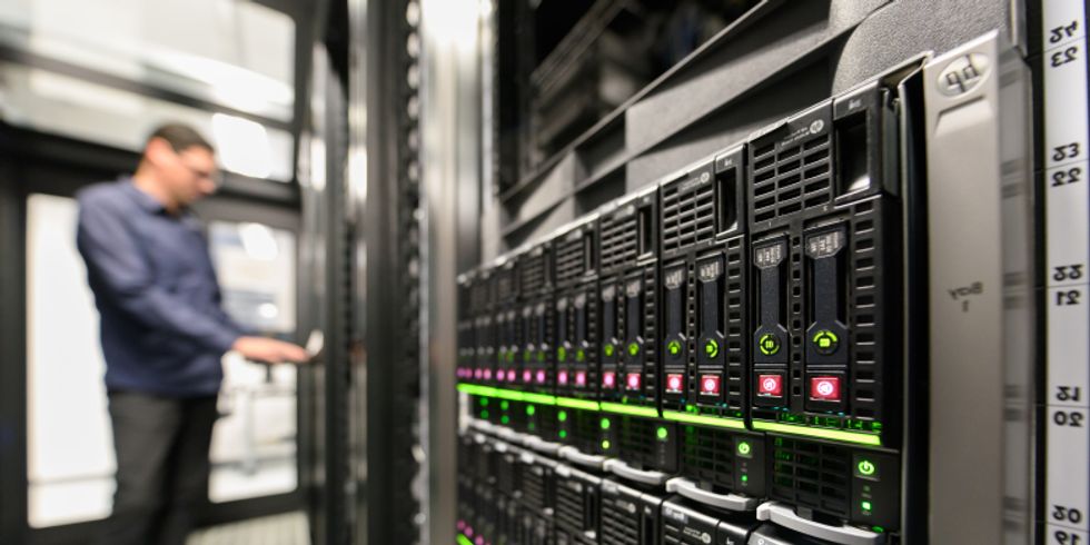 Ein Mitarbeiter in unscharf links im bild, steht an einem Terminal welches in einer reihe von Serverschränken sich befindet.