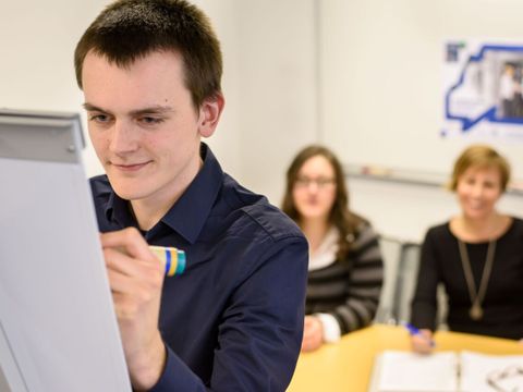 Ein Mitarbeiter schreibt auf ein Whiteboard vor zwei anderen Mitarbeitern
