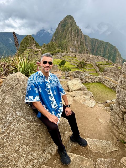 Person sitzt vor der historischen Ruinenstadt Machu Picchu in Peru mit Berglandschaft im Hintergrund.