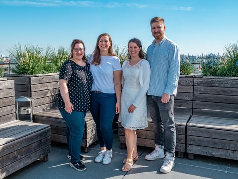 Gruppenfoto der Ausbildungsleitung des ITDZ Berlin auf einer Dachterrasse. Vier Personen stehen lächelnd vor Pflanzenkübeln und Sitzbänken, im Hintergrund ist die Berliner Stadtlandschaft zu sehen.