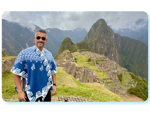 Person sitzt vor der historischen Ruinenstadt Machu Picchu in Peru mit Berglandschaft im Hintergrund.