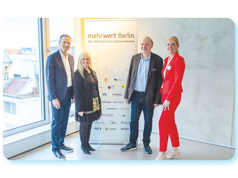 Vier Personen stehen bei einer Veranstaltung neben einem Roll-up-Banner mit der Aufschrift „mehrwert Berlin“.