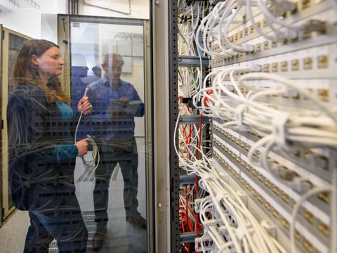 Zwei Mitarbeitende des ITDZ-Berlin schauen sich einen Netzwerkschrank an.