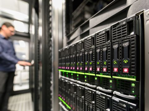 Ein Mitarbeiter in unscharf links im bild, steht an einem Terminal welches in einer reihe von Serverschränken sich befindet.
