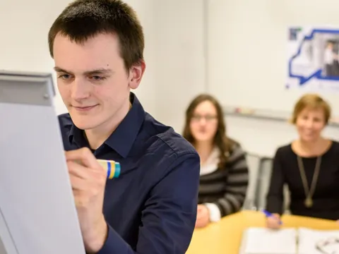 Ein Mitarbeiter schreibt auf ein Whiteboard vor zwei anderen Mitarbeitern