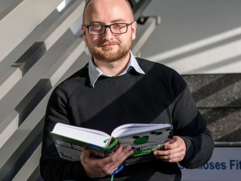 Eine lächelndee Mitarbeiterin des ITDZ-Berlin hält ein Buch in der Hand im Treppenhaus.