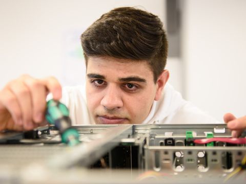 "Ahmad" arbeitet konzentriert an einem Computer Gehäuse.