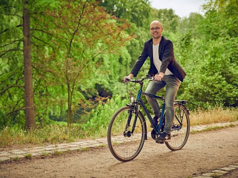 Ein Fahrradfahrer fährt auf einem Sandweg. Im Hintergrund ist Wald.
