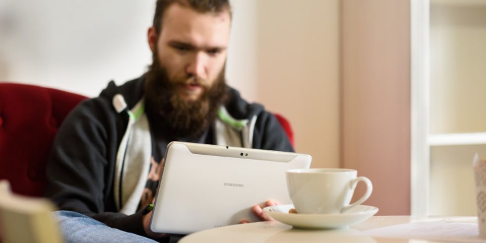 Person sitzt in einem Kaffee und schaut auf sein Tablet