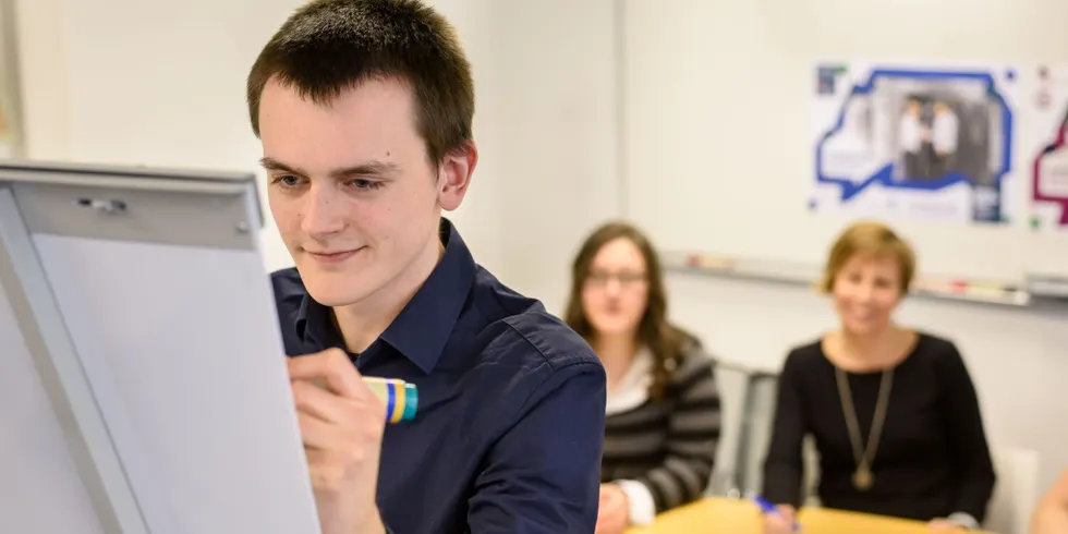 Ein Mitarbeiter schreibt auf ein Whiteboard vor zwei anderen Mitarbeitern