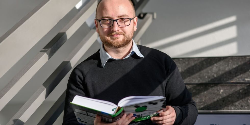 Eine lächelndee Mitarbeiterin des ITDZ-Berlin hält ein Buch in der Hand im Treppenhaus.