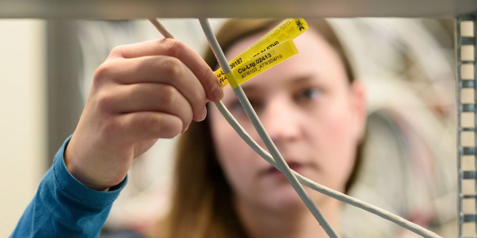 Eine Mitarbeitende überprüft Kabel aus einem Serverschrank anhand eines gelben Etikets.