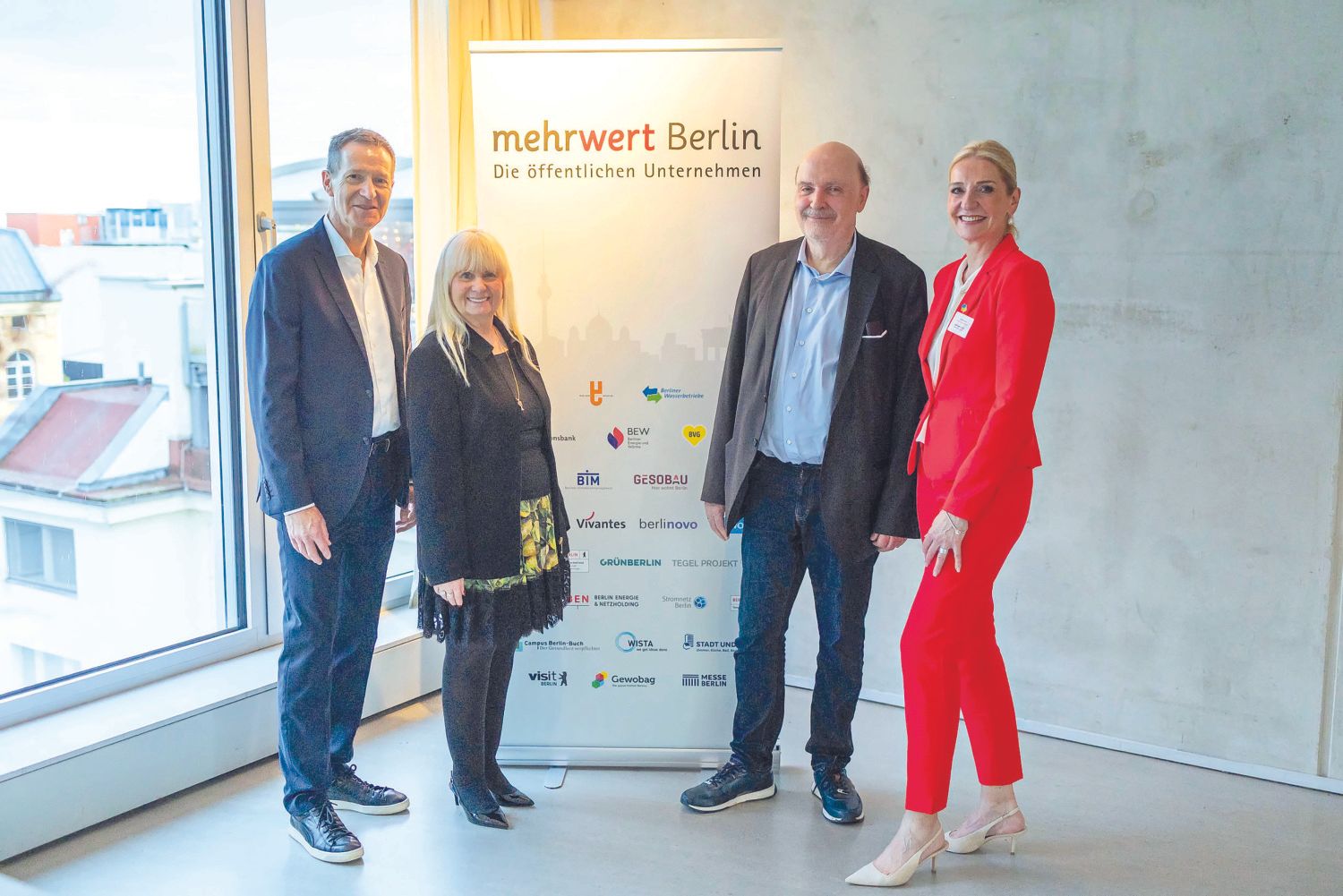 Vier Personen stehen bei einer Veranstaltung neben einem Roll-up-Banner mit der Aufschrift „mehrwert Berlin“.