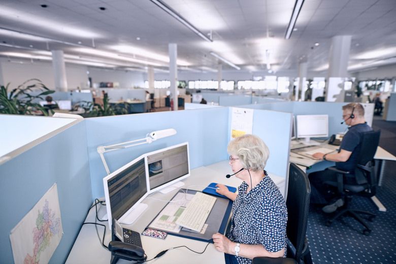 Zwei Personen sitzen an ihren Arbeitsplätzen in einem Großraumbüro mit Head Set und telefonieren