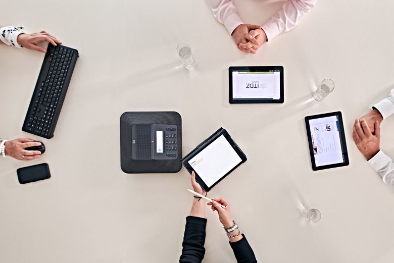 Tablets, Tastatur, Maus und mehrere Arme von Peronen auf einem Tisch