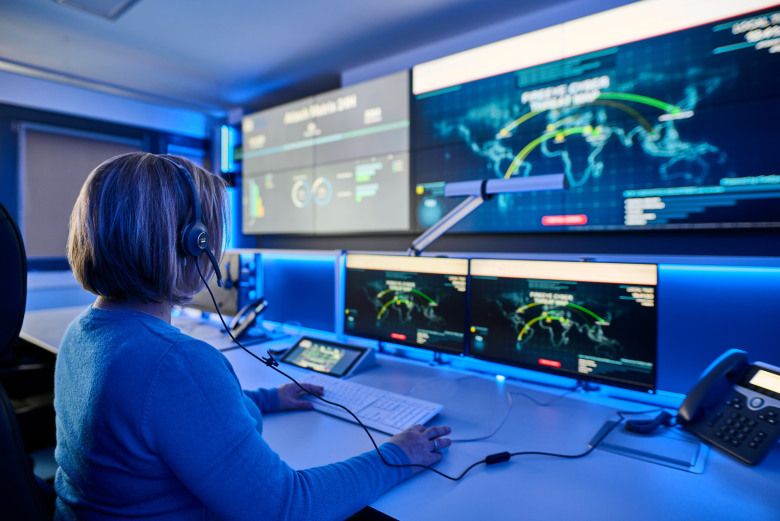 Frau sitzt vor mehreren großen Monitoren