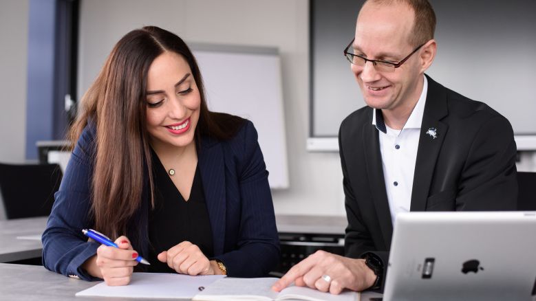 Zwei Personen sitzen am Tisch und schauen auf einen Laptop