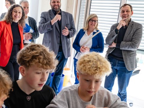 Im Vordergrund Schüler vor einem Laptop, im Hintergrund Erwachsene, die lächelnd zuschauen
