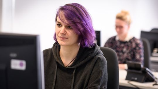 junge Frau mit lila Haaren sitzt vor einem Monitor