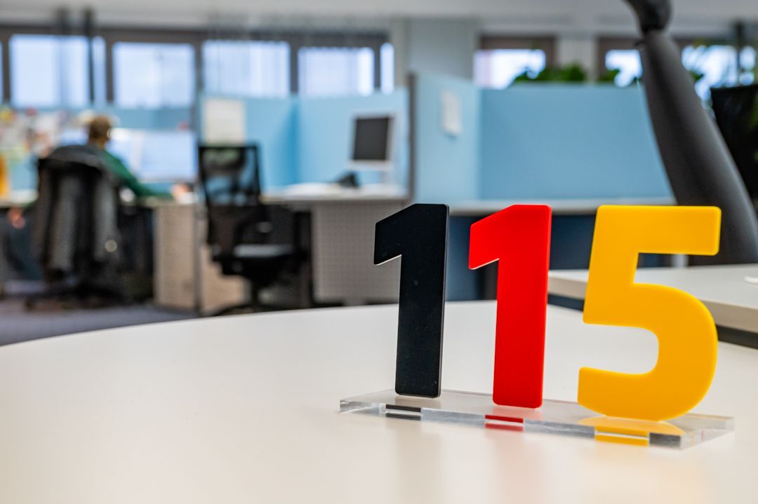 Kleiner Aufsteller mit 115 auf einem Tisch, dahinter verschwommen das Callcenter
