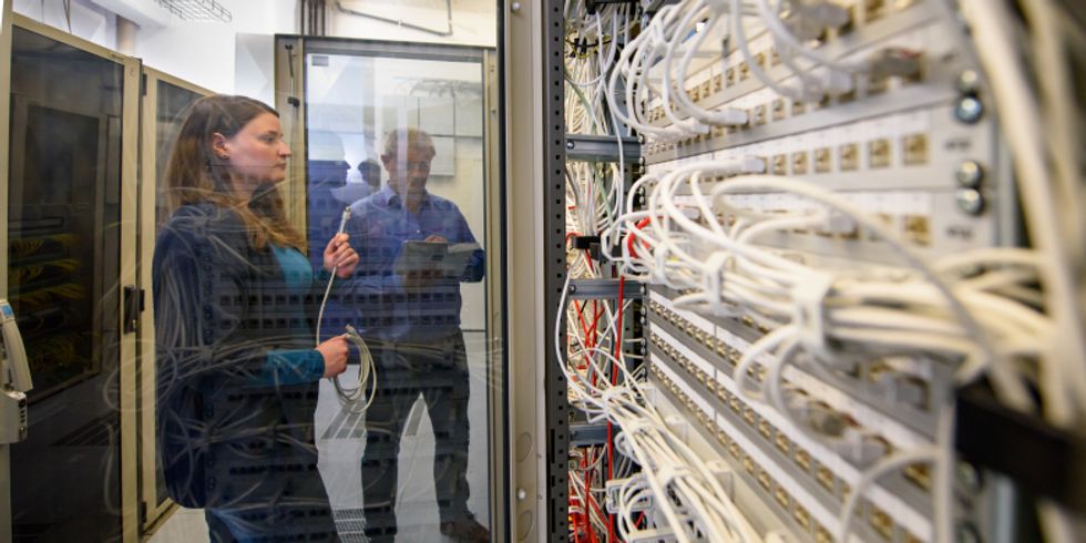 Zwei Mitarbeitende des ITDZ-Berlin schauen sich einen Netzwerkschrank an.