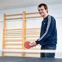 Bildvergrößerung: junger Mann steht lachend an einer Tischtennisplatte mit Schläger und Ball in der Hand