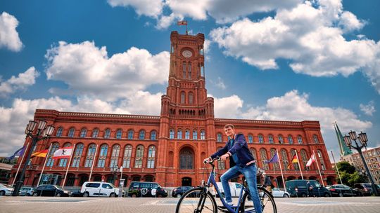 Ein Mann sitzt auf einem Fahrrad. Im Hintergrund ist das rote Rathaus zu sehen.