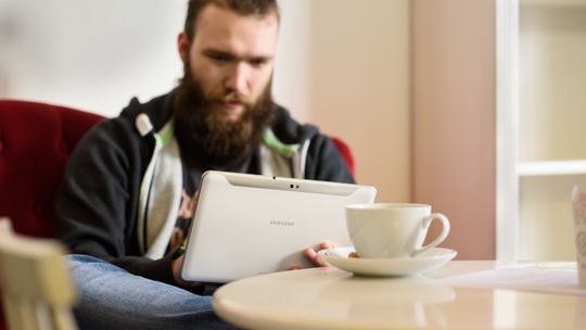 Person sitzt in einem Kaffee und schaut auf sein Tablet