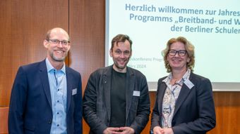 Ralf Brüchmann, Dr. Torsten Kühne und Anne Lolas stehen vor der Präsentation