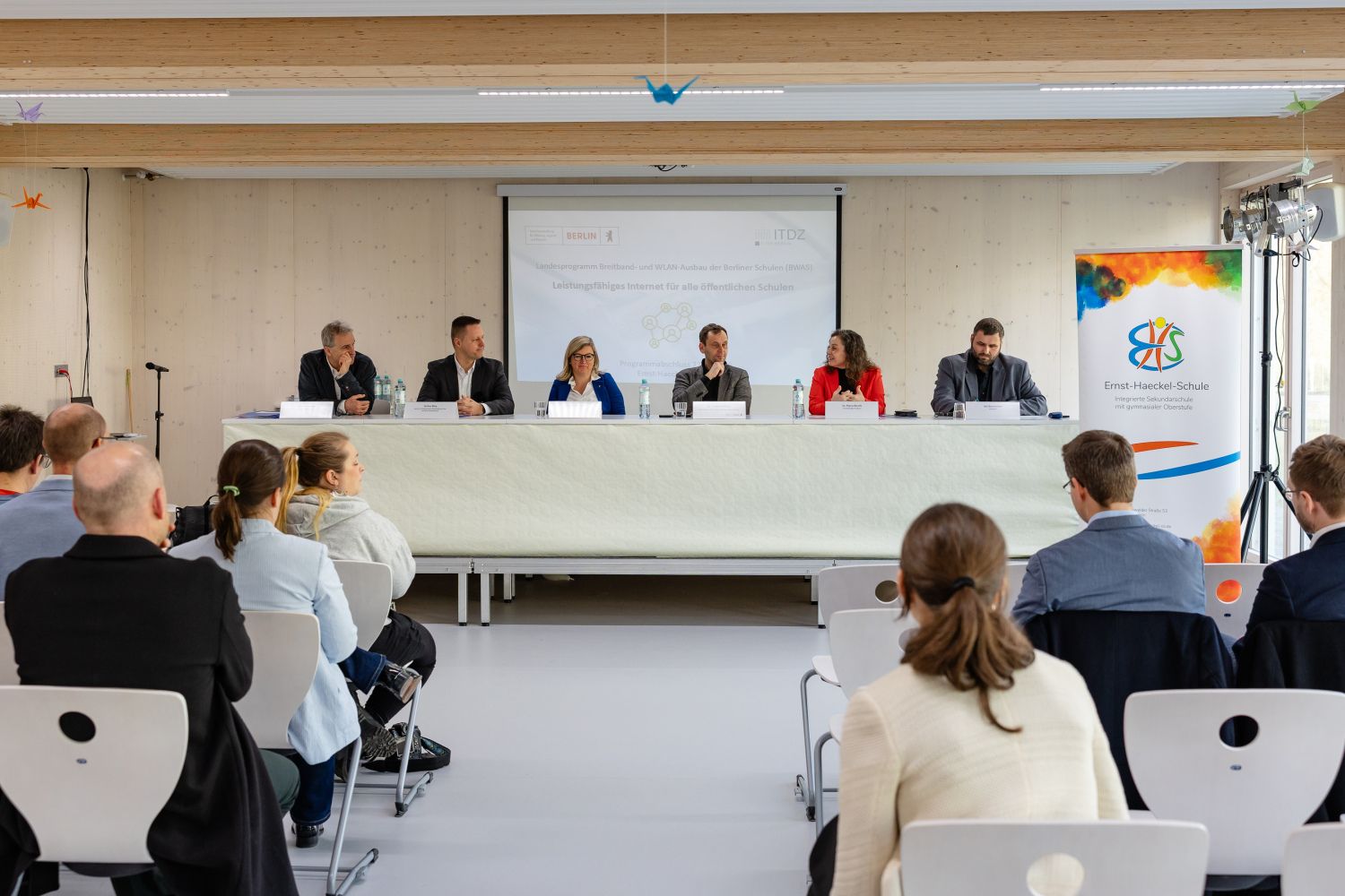 Pressekonferenz, bei der mehrere Personen an einemTisch sitzen, davor Publikum auf Stühlen
